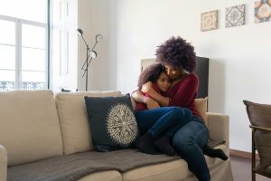 A loving mother embraces her daughter on a cozy sofa at home, creating a warm and affectionate family moment.